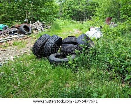 An abandoned lot of land in rural Nova Scotia where garbage is disposed of illegally. The trash includes tires, old cars, planks of wood, and other unusable items related to transportation. Royalty-Free Stock Photo #1996479671