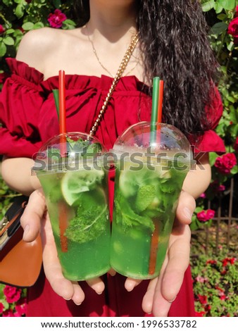 Woman in red sundress holding two cool glasses with mojito