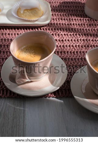 Closeup view of an elegant white ceramic cup of coffee over a pinkish tablecloth.
