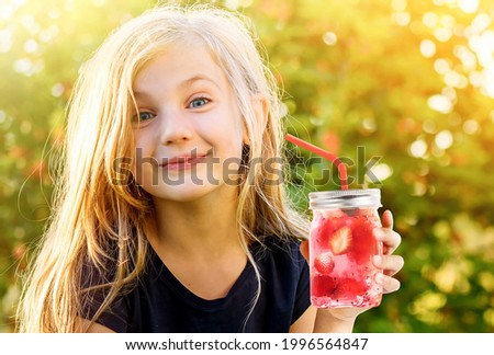 Cute funny little girl with frozen strawberry cocktail in drinking mason jar at sunset.