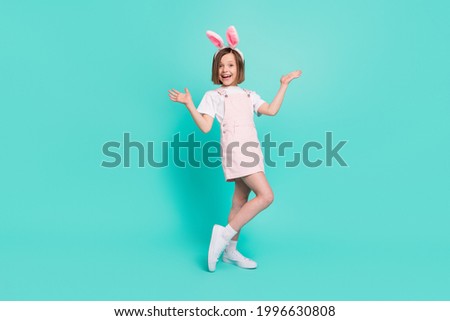 Photo of funky impressed school girl wear pink overall bunny ears smiling rising arms isolated teal color background
