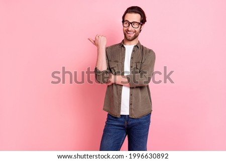 Photo of pretty cute young guy dressed brown shirt eyeglasses looking pointing thumb up empty space isolated pink color background
