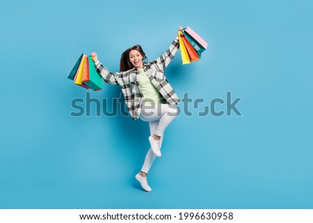 Full size photo of positive happy young woman jump up winner hold bags shop isolated on blue color background