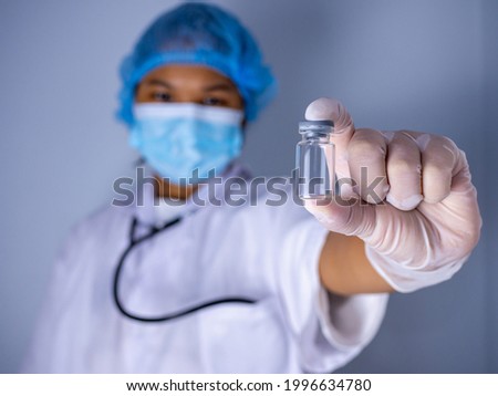 Studio portrait of a female doctor wearing a mask and wearing a hat. in the hand of the vaccine bottle and stretched out his arms in front standing on a white background. studio shot background.