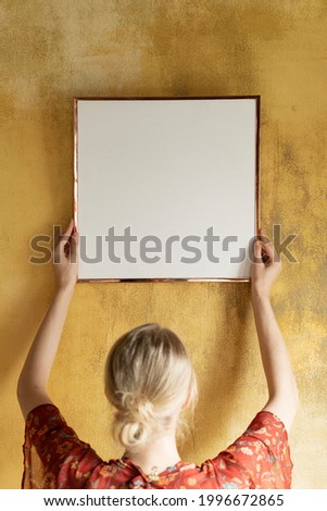 Woman hanging a frame mockup on a grunge yellow wall