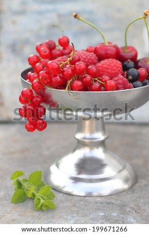 berries currants, raspberries, cherries in a metal vase on the leg