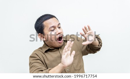Wow and shocked face expression of young Asian Malay man in casual shirt with both hand upward looking on empty space on isolated white background.