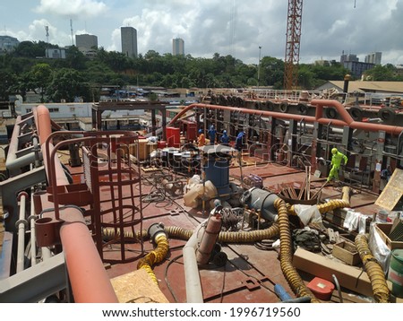 Picture of repairs, maintenance, modifications ongoing on a vessel main deck in a ship yard. Lot of equipment installed creating a difficult working environment. Safety at work. Royalty-Free Stock Photo #1996719560
