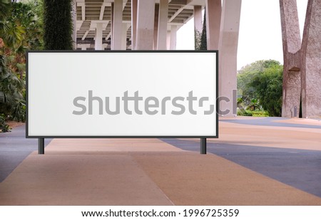 Blank large billboard advertising banner mockup in a large open space with plants under a modern bridge. Large horizontal digital display screen, an out-of-home OOH media display space Royalty-Free Stock Photo #1996725359