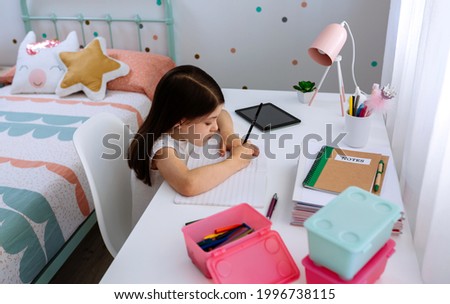 Girl doing homework sitting at a desk in her bedroom Royalty-Free Stock Photo #1996738115