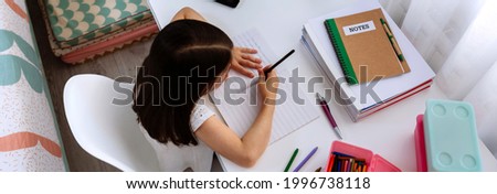 Top view of unrecognizable girl doing homework sitting at a desk in her bedroom