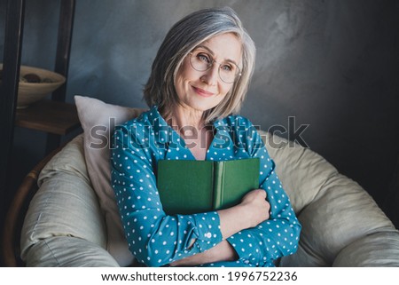 Photo of cheerful nice old lady hug book sit wear blue shirt at home alone Royalty-Free Stock Photo #1996752236