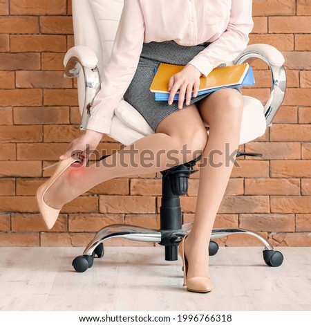 Young woman feeling ache because of wearing uncomfortable shoes in office