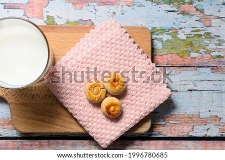 Traditional Malay crunchy peanut cookies, locally known as "Biskut Kacang", lying on cutting board; with decorations (a glass of milk and pink napkin). A selective focus photo of the cookies.