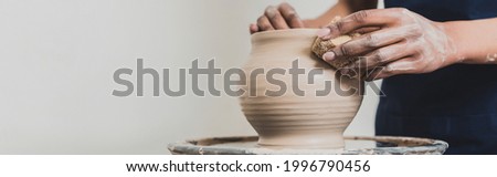 partial view of young african american woman modeling wet clay pot on wheel with sponge in pottery, banner Royalty-Free Stock Photo #1996790456