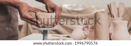 partial view of young african american man sculpting clay pot with hands on table with equipment in pottery, banner