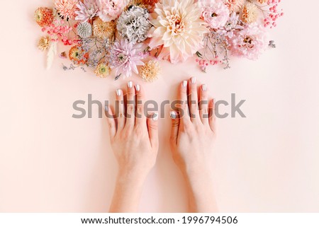 Top view of crop unrecognizable female with blooming flowers demonstrating stylish neat manicure on pink background