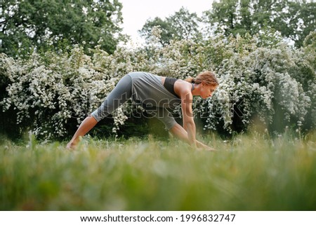 A young woman goes in for sports in the park standing on the green grass, performs yoga exercises for the lumbar spine. Royalty-Free Stock Photo #1996832747