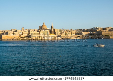 Landscape of Valetta skyline in Malta with boat passing. The stunning skyline of old Valletta, its churches and towers, its historic remparts from the Northern Harbour on golden hour.