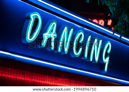 Low angle of vivid neon sign of dancing illuminated by blue and purple colors over entrance at night