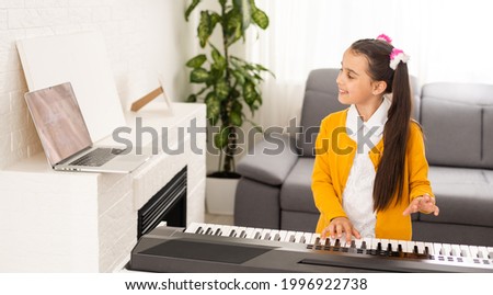 Homeschool little young kid girl learning piano from computer connecting to internet music online class by school teacher. New normal lifestyle and education, student study at home concept.