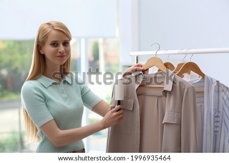 Young woman cleaning clothes with lint roller indoors
