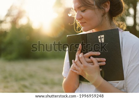 Christian woman holds bible in her hands. Reading the Holy Bible in a field during beautiful sunset. Concept for faith, spirituality and religion. Peace, hope Royalty-Free Stock Photo #1996959248