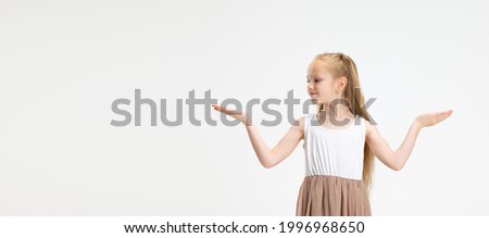 Pointing. Half length portrait of cute little Caucasian gir with long hair in stylish dress posing isolated on white studio background. Happy childhood, emotions, facial expression concept. Flyer