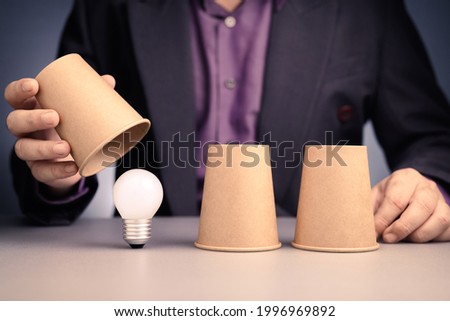 Man play a three cups shell game and reveal the right one to find a light bulb