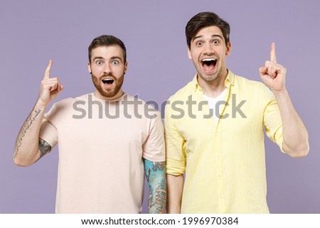 Two young excited men friends together in casual t-shirt tattoo translate fun holding index finger up with great new idea isolated on purple color background studio portrait People lifestyle concept.