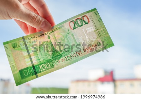 Hand holds russian bank note two hundred rubles against the window. Watermarks detected
