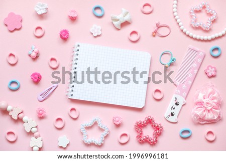 Blank notepad, cute comb with kawaii cat face and kid's hair accessories on pink pastel background