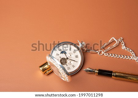 Fountain pen and clock, beautiful details of a fountain pen and an antique clock exposed on a leather surface, selective focus.