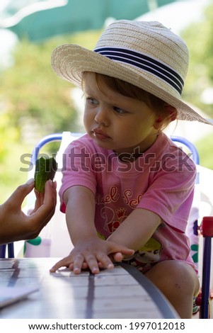 An emotional charming girl in a hat of two years eats and watches cartoons. A large portrait.