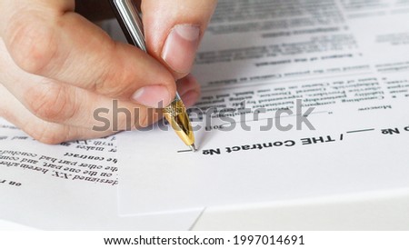 A businessman sitting at an office desk signs a contract with a shallow emphasis on signing. business and finance