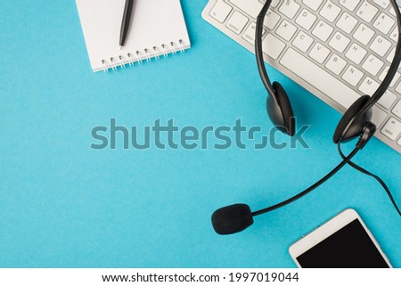Top view photo of black headset on white keyboard pen on notebook and mobile phone on isolated pastel blue background with blank space