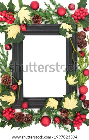 Winter greenery abstract border with wooden frame, red bauble decorations, holly and winter greenery on white background. Festive composition for the solstice and Christmas holiday season. Copy space.