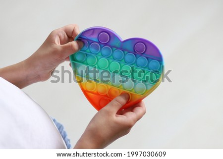 A trendy anti-stress pop-it toy in the shape of a heart in a child's hand. Top view. Selective focus. Concept: rainbow anti-stress toy simple dimple.