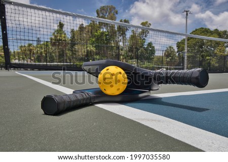 Closeup of a pickleball and paddles on an empty court under sunny skies. Royalty-Free Stock Photo #1997035580