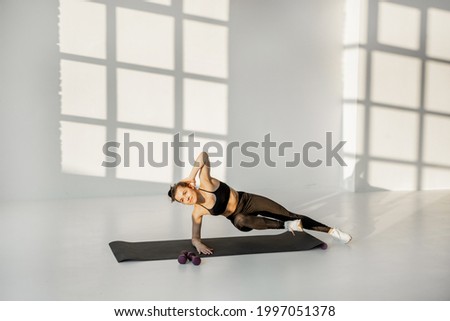 Athletic woman stands in the plank on a fitness matt, performing static exercise on a fitness training at white room alone