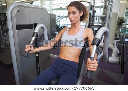 Fit woman using the weights machine for her arms at the gym