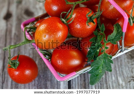 A shopping basket filled with cherry tomatoes on a wooden background.