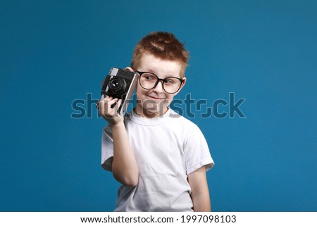 Little boy taking a picture using a retro camera. Child boy with vintage photo camera isolated on blue background. Old technology concept with copy space. Child learning photography .