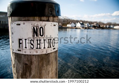 No fishing sign in front of clear blue lake with houses in the distance 