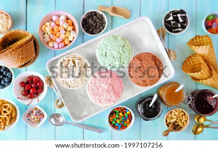 Summer ice cream buffet with a variety of flavors and sweet toppings. Overhead view table scene on a blue wood background.
