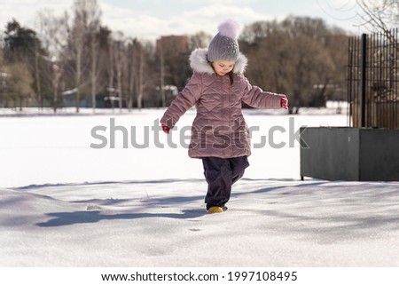 playful little girl walking in a snowy park on a winter sunny day