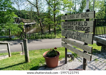 Harpersfield Covered Bridge Sign With Historic Structure In Background.