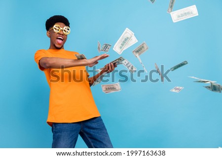 Photo of young happy dark skin crazy man fly money rain wear funny glasses isolated on blue color background