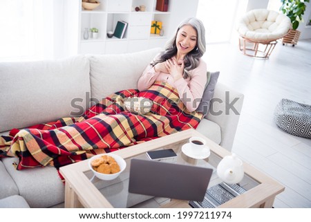 Full body photo of happy positive old lady look laptop watch film good mood eat pop corn indoors inside house
