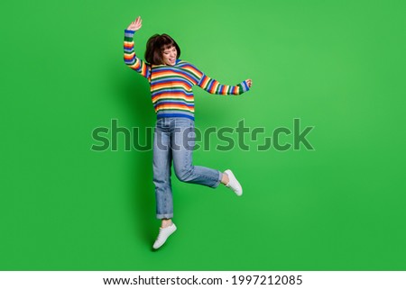 Full length photo of pretty funky young woman wear striped sweater smiling jumping high isolated green color background